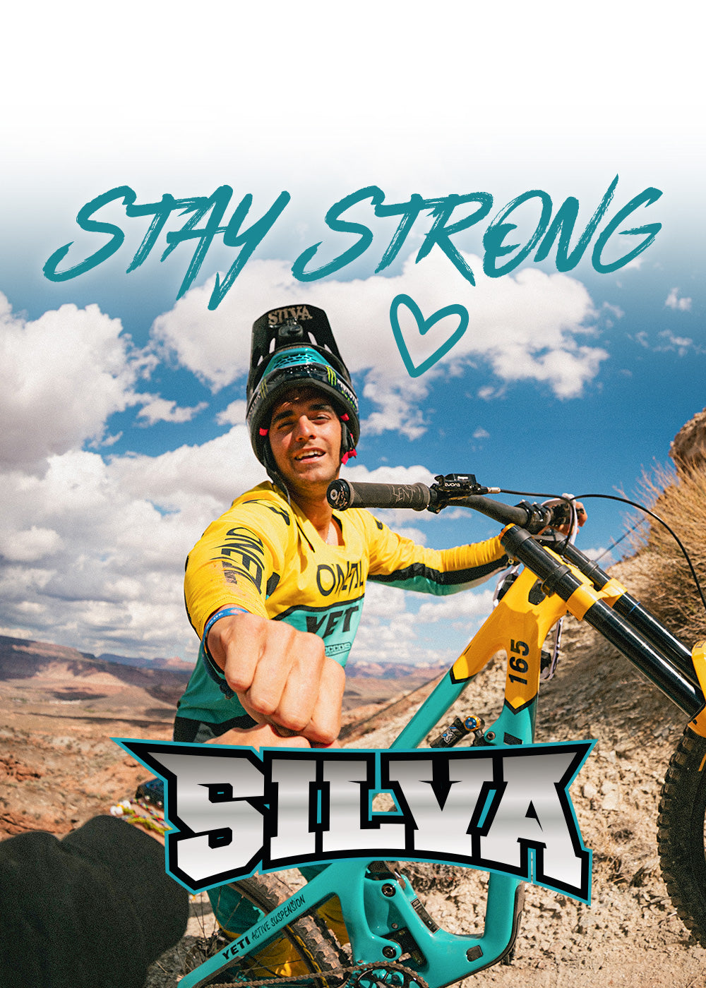 Ein Mountainbiker in gelber Montur stößt mit der Faust in die Kamera und lächelt neben seinem Fahrrad. Blauer Himmel und felsige Landschaft im Hintergrund. Der Text "STAY STRONG" und ein Herz sind über ihm, mit "SILVA" am unteren Rand.