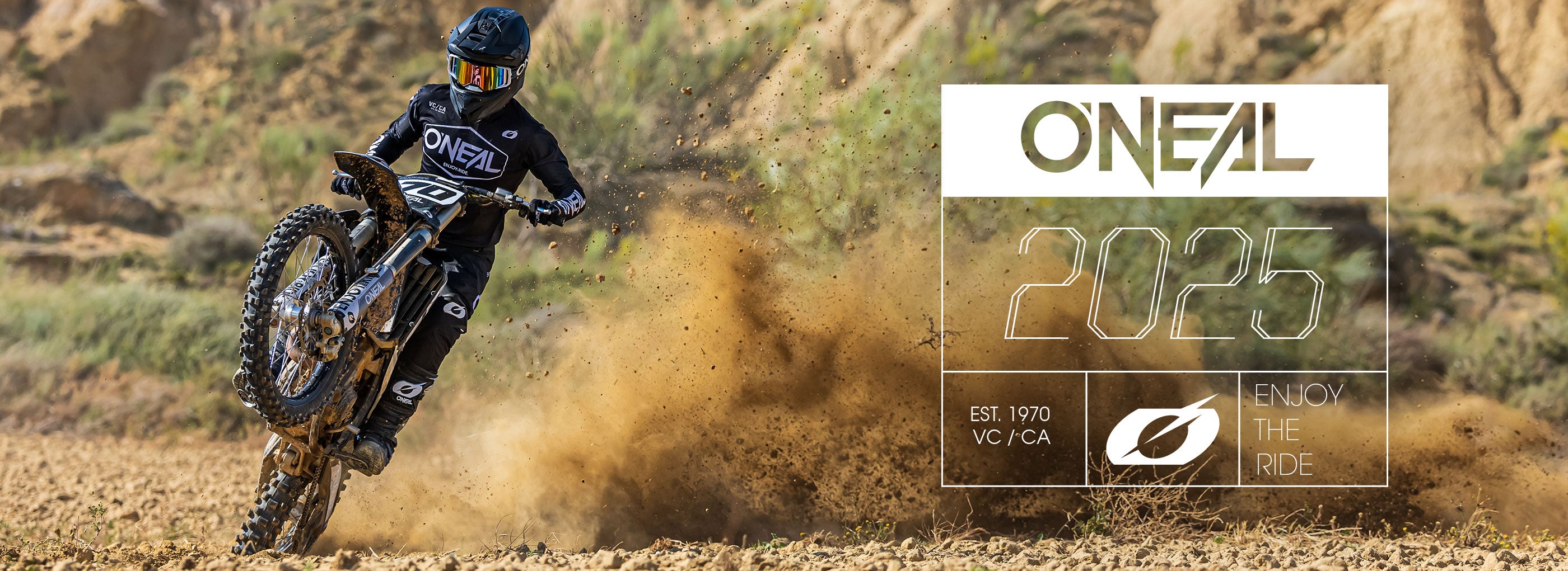 Ein Motocross-Fahrer in schwarzer O’Neal-Ausrüstung macht auf seinem Dirtbike einen Wheelie und wirbelt dabei Staub auf. Rechts steht „O’NEAL 2025“, „Est. 1970“ und „Enjoy the Ride“.