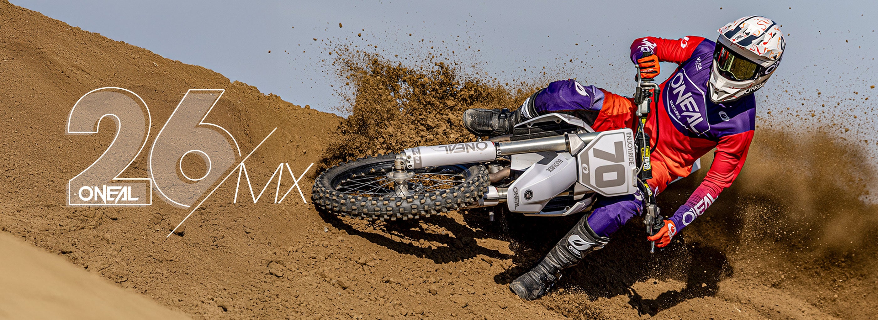 Ein Motocross-Fahrer in einem roten und lila O'NEAL-Anzug und -Helm lehnt sich scharf auf einer Schotterpiste an und wirbelt Staub auf, daneben steht in großer Schrift "26% MX" und links das O'NEAL-Logo.