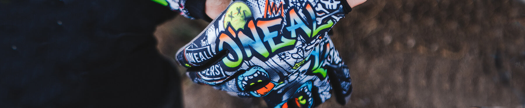 Nahaufnahme einer behandschuhten Hand, die einen bunten Handschuh mit Graffitimuster trägt, auf dem das Wort „O’NEAL“ und verschiedene abstrakte Designs in Grün, Orange und Weiß auf dunklem Hintergrund zu sehen sind.