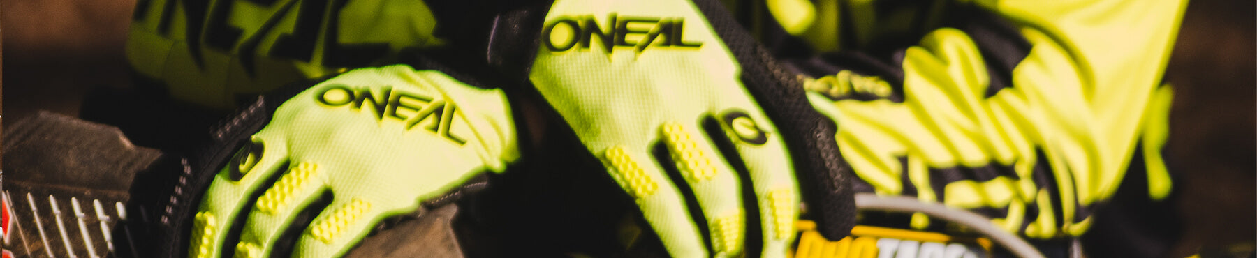 Nahaufnahme einer Person, die leuchtend gelbe O'Neal-Motocross-Handschuhe trägt und ihre Hände auf dem Lenker eines Sportmotorrads ruhen lässt.