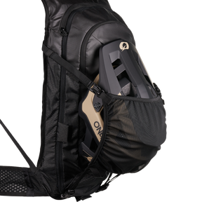 Nahaufnahme des O'NEAL JUNCTION MTB Protektorrucksack von O'NEAL Europe, die eine Netztasche mit einem grauen und beigen Fahrradhelm zeigt. Der Rucksack verfügt über gepolsterte Gurte, eine strukturierte Seitenwand und verbesserte Schutzfunktionen.
