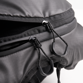 Nahaufnahme des Doppelreißverschlusses des O'NEAL Europe JUNCTION MTB Protektorrucksacks, teilweise geöffnet, um das strukturierte Gewebe und die robusten Reißverschlüsse mit Schlaufen zum einfachen Greifen zu zeigen.
