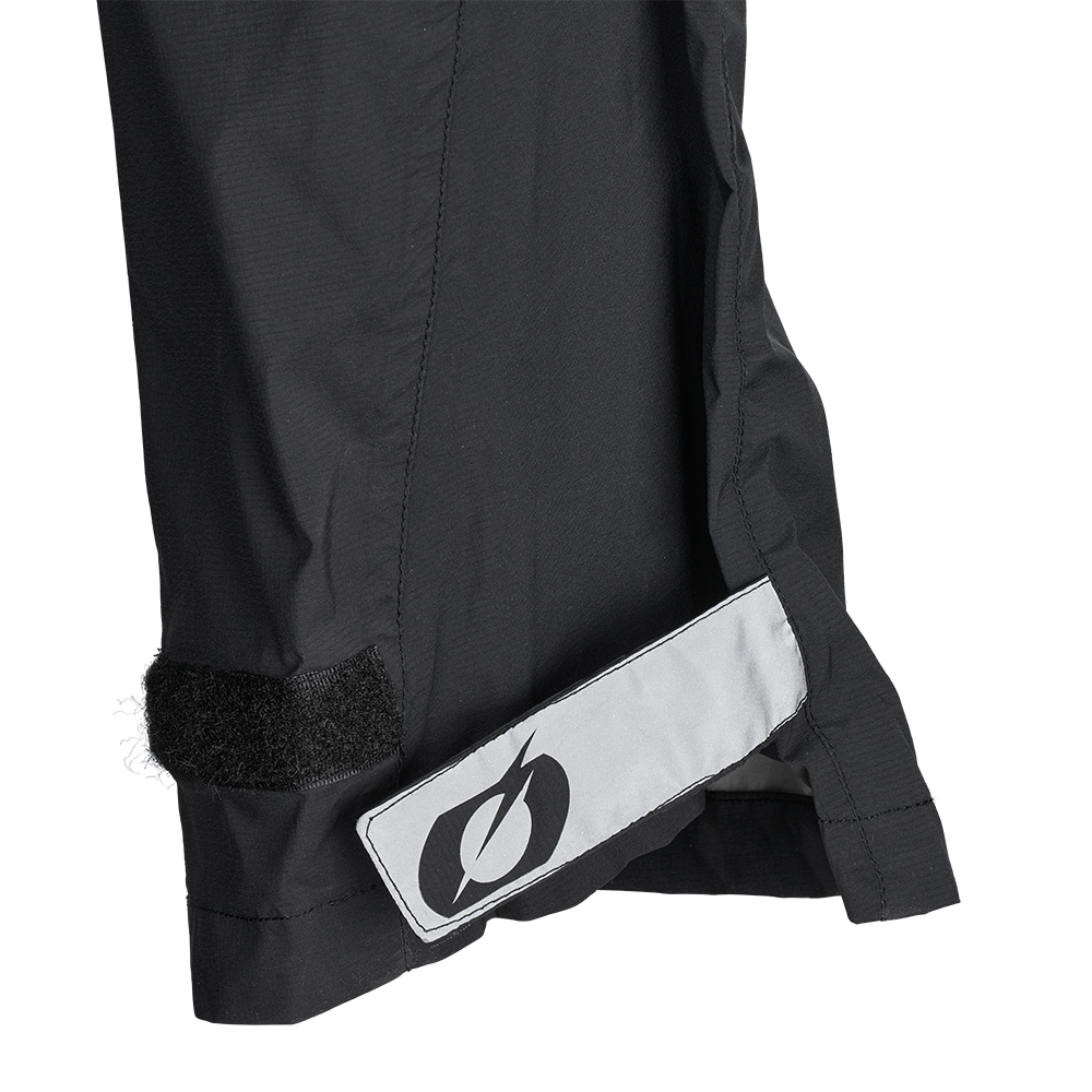 Nahaufnahme einer schwarzen O'NEAL TORRENT Regenhose mit Klettverschluss und reflektierendem Blitz-Patch, ideal als atmungsaktive Regenhose für den Radsport, abgebildet auf weiß.