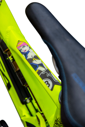 Close-up of a neon yellow AZONIC bicycle frame with a black saddle, with AZONIC FRAME GUARDS and a cartoon graphic of a woman with pink hair and a blue outfit on a bicycle.