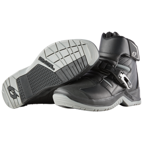 Une paire de bottes O'NEAL RMX SHORTY en noir et gris - une botte debout, l'autre sur le côté pour montrer la semelle structurée et la boucle de fermeture - idéal pour un port confortable sur la moto.