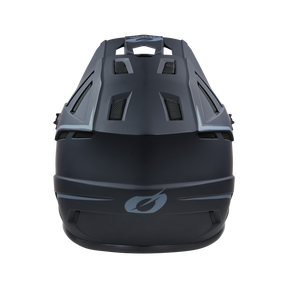 Ein schwarzer O'NEAL BACKFLIP Helm SOLID mit Lüftungsschlitzen und einem weißen stilisierten Logo auf der Vorderseite, frontal vor einem schwarzen Hintergrund.