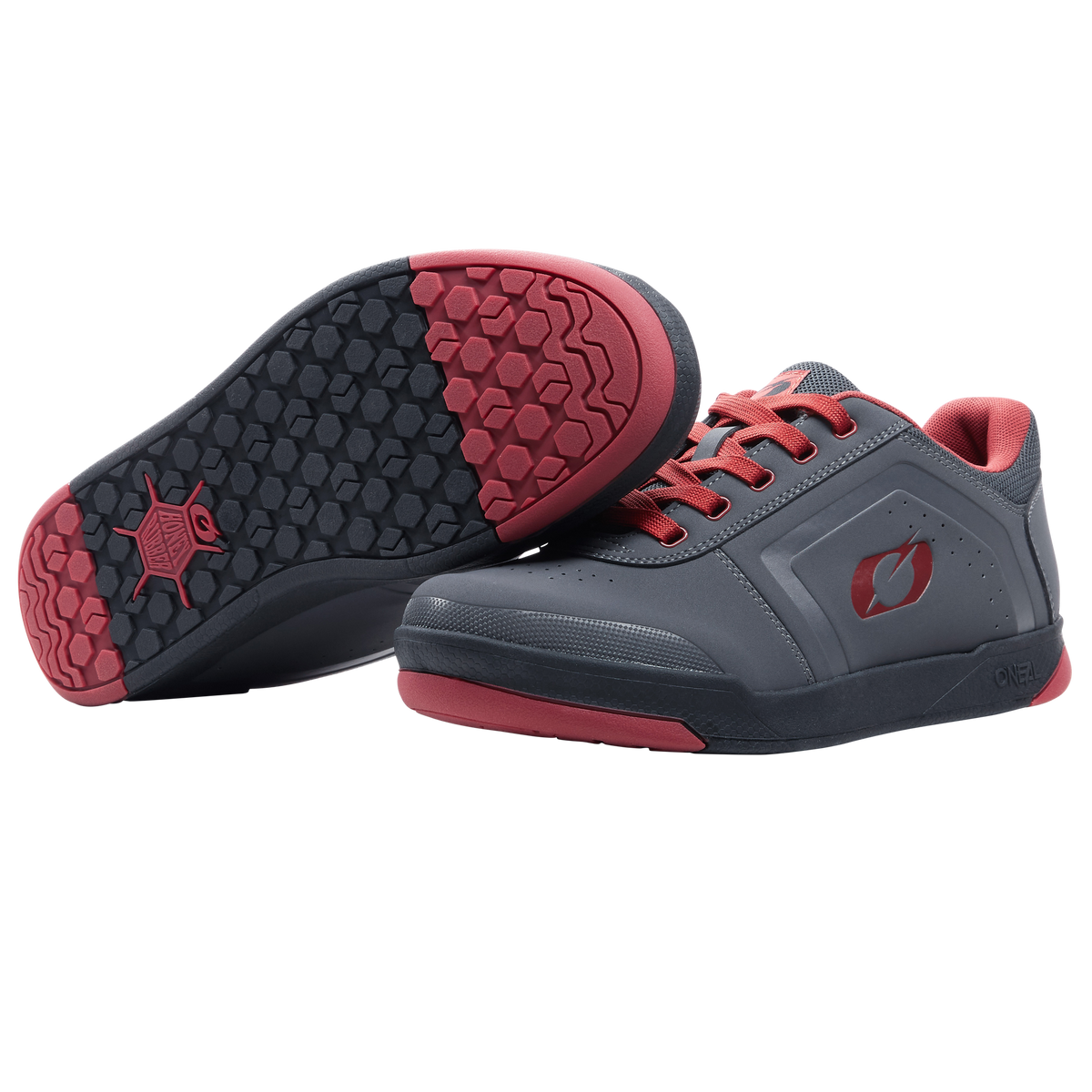 Ein Paar O'NEAL PINNED FLAT Pedal Schuhe in Grau mit roten Sohlen und Schnürsenkeln. Ein Schuh steht aufrecht, während der andere ein schwarzes und rotes Profil aufweist, das bei Fahrten mit flachen Pedalen optimalen Halt bietet. Marke: O'NEAL.