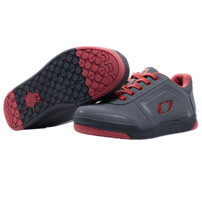 A pair of O'NEAL PINNED FLAT pedal shoes in gray with red soles and laces. One shoe stands upright, while the other has a black and red profile that offers optimum grip when riding with flat pedals. Brand: O'NEAL.