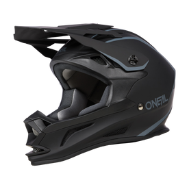 Le casque O'NEAL DROP DH SOLID est un casque intégral noir mat avec des accents gris-bleu. Il dispose d'une visière carrée et d'un protège-menton sur le côté duquel on peut voir le nom de la marque "O'NEAL" en blanc. Ce casque aérodynamique est conçu pour le vélo tout-terrain et offre à la fois sécurité et confort.
