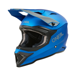 Der O'NEAL 1SRS Helm SOLID, ein blauer MX-Helm mit Visier und schwarz-grauen Details, verfügt über Belüftungsöffnungen und überlegene Technik - alles vor einem schwarzen Hintergrund.