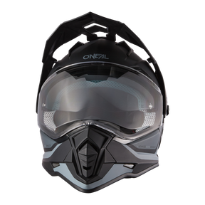 Vista frontal del casco Sierra R de O'NEAL, un casco de ciclismo negro y gris con visera transparente, diseño angular y funciones de ventilación, mostrado sobre un fondo negro liso.