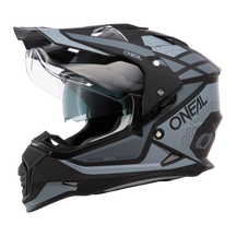 El casco Sierra R de O'NEAL en negro y gris con visera transparente, diseño angular y aberturas de ventilación detalladas se muestra de perfil sobre fondo blanco.
