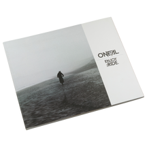 The closed O'NEAL ENJOY THE RIDE BOOK shows a lonely figure on a foggy beach that evokes emotions. The O'NEAL logo and the words "ENJOY THE RIDE." in black on white can be seen on the right-hand side. Brand: O'NEAL. Product: O'NEAL ENJOY THE RIDE BOOK (FREE GOODIE WAGON).
