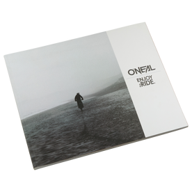 The closed O'NEAL ENJOY THE RIDE BOOK shows a lonely figure on a foggy beach that evokes emotions. The O'NEAL logo and the words "ENJOY THE RIDE." in black on white can be seen on the right-hand side. Brand: O'NEAL. Product: O'NEAL ENJOY THE RIDE BOOK (FREE GOODIE WAGON).