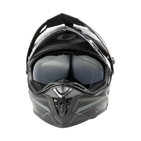 Un O'NEAL A-SRS Helmet SOLID gris mat, un casque de moto en fibre de verre avec une visière claire, des ouvertures d'aération noires, un design anguleux et des fonctions compatibles Bluetooth, est représenté de face sur un fond noir.