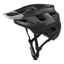 El casco O'NEAL Defender Solid en negro mate y gris tiene visera, varios orificios de ventilación y barboquejos ajustables -ideal para la conducción all-mountain- y está ilustrado sobre un fondo blanco liso.