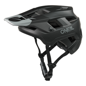 El casco O'NEAL Defender Solid en negro mate y gris tiene visera, varios orificios de ventilación y barboquejos ajustables -ideal para la conducción all-mountain- y está ilustrado sobre un fondo blanco liso.