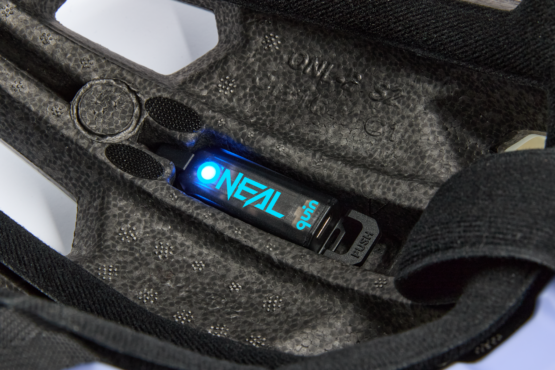 Die Nahaufnahme der Innenseite des O'NEAL TRAILFINDER EVO Helms SOLID zeigt einen blau leuchtenden Quin Smart Safety Sensor mit der Aufschrift "O'NEAL quin", der fest mit der Schaumstoffpolsterung verbunden ist.