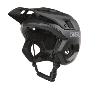 A black O'NEAL TRAPPER Helmet SOLID mountain bike helmet with visor, side vents, padded interior and adjustable chin strap is shown from the side on a solid color background.