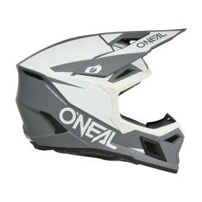 Un casco da motocross integrale O'NEAL 3SRS Solid, grigio e bianco, con un'ampia visiera, aperture di ventilazione aerodinamiche e una robusta mentoniera, mostrato di lato su uno sfondo trasparente.