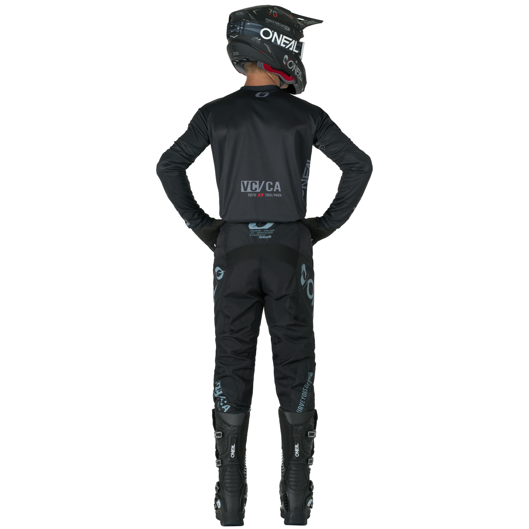 Eine Person in schwarzer O'NEAL ELEMENT-Hose, Helm, Handschuhen und Stiefeln steht mit den Händen auf den Hüften und schaut weg. Die Logos der Marke O'NEAL sind auf dem Anzug und dem Helm sichtbar.