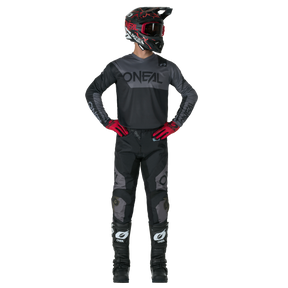 A person in a complete motocross outfit, consisting of black O'NEAL ELEMENT PANTS RACEWEAR, a black O'NEAL helmet, jersey, red gloves and black boots, stands with hands on hips in front of a plain background.