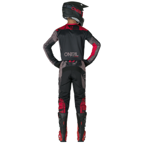 A person in black and red O'NEAL ELEMENT Pants ROLLER motocross gear, helmet and boots stands facing away from the camera with his hands on his hips. The "O'NEAL" logo can be seen on the back of the outfit.
