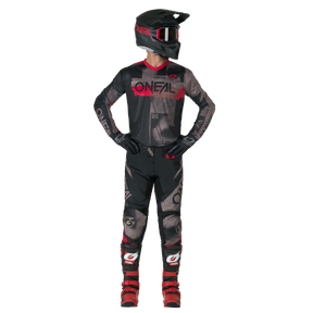 A person in full motocross gear - black and red O'NEAL jersey, gloves, red boots and O'NEAL ELEMENT Pants ROLLER - stands there and looks to the side.