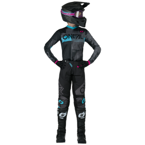 Una persona vestida con el pantalón de mujer O'NEAL Element ROLLER by O'NEAL, un casco negro con gafas, un maillot negro y azul, guantes negros con detalles rosas y botas negras de motocross está de pie con las manos en las caderas.