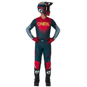 Una persona con un atuendo completo de motocross, compuesto por unos pantalones O'NEAL Hardwear SWIPE y un maillot, guantes, botas y casco a juego, está de pie con las manos en las caderas y mira a un lado.