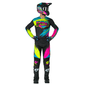 Ein Motocross-Fahrer in voller Montur, mit schwarzem Helm und O'NEAL MAYHEM Pants RESEDA mit leuchtenden neonblauen, gelben und pinken Akzenten, steht mit sichtbarem O'NEAL-Branding an der Seite.