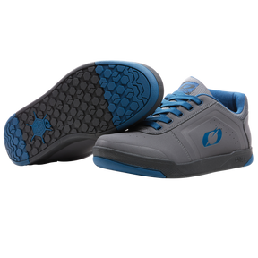 Un par de zapatillas de pedal O'NEAL Pinned PRO FLAT en gris con detalles azules, cordones y logotipo. Ideales como accesorios para bicicleta de montaña: una zapatilla vertical y la otra con suela texturizada en negro y azul. Marca: O'NEAL.