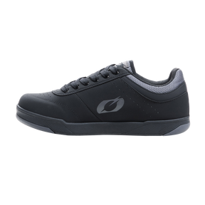La chaussure O'NEAL PUMPS FLAT est une chaussure de cyclisme noire et plate avec des accents gris, une semelle structurée, un logo stylisé sur le côté et des lacets noirs. Représentée de côté sur un fond blanc simple.