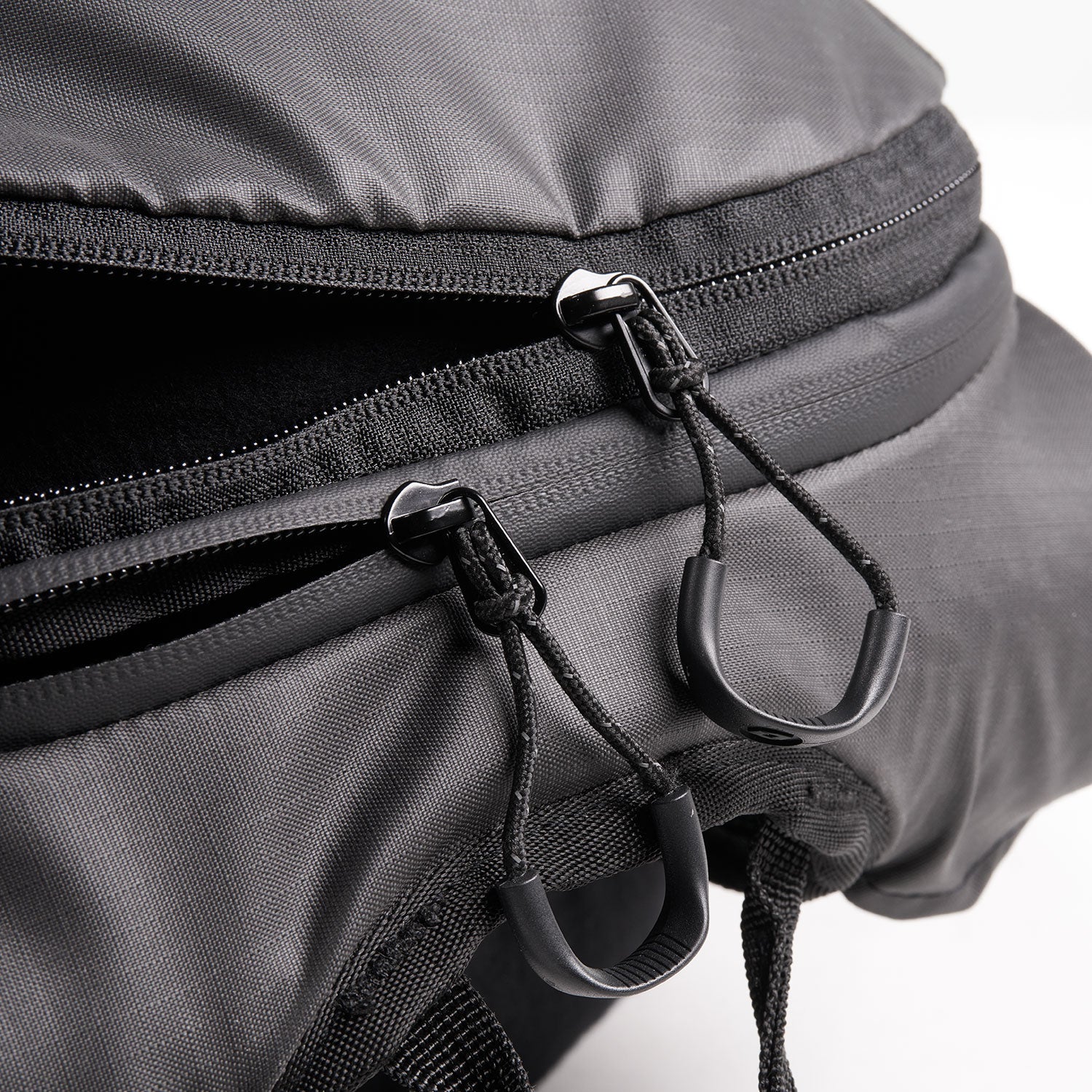 Nahaufnahme eines schwarzen Rucksacks mit zwei Reißverschlüssen, die teilweise geöffnet sind und den Blick auf das Innenfach freigeben, vor einem weißen Hintergrund.