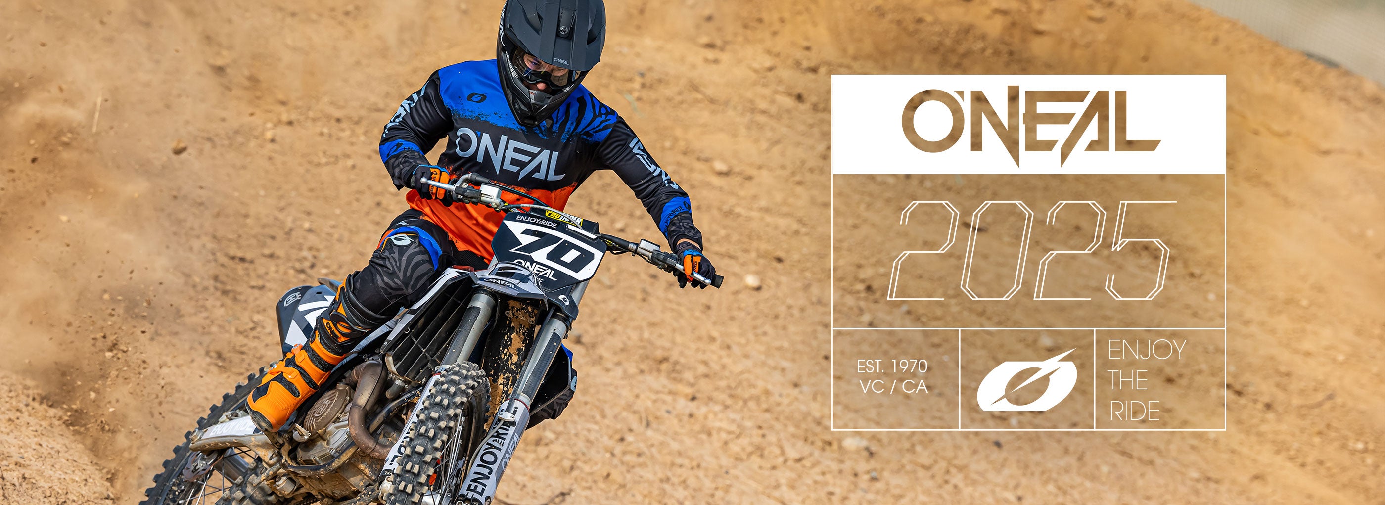 Ein Motocross-Fahrer in blau-orangefarbener O'NEAL-Ausrüstung fährt mit einem Dirtbike auf einer Sandpiste. Die Textüberlagerung lautet „O'NEAL 2025“, „EST. 1970, VCY/CA“ und „ENJOY THE RIDE“ mit einem stilisierten Blattsymbol.