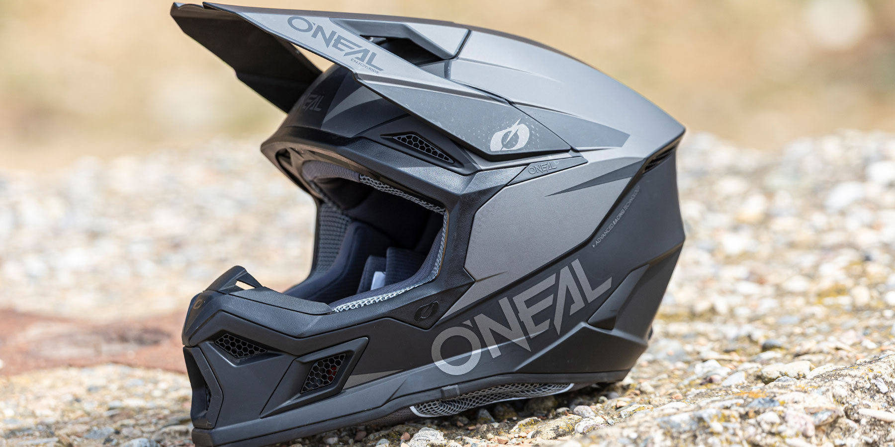 Ein mattschwarzer O'Neal-Mountainbike-Vollvisierhelm mit kantigem Design und Belüftungsöffnungen ruht auf einer Kiesfläche.