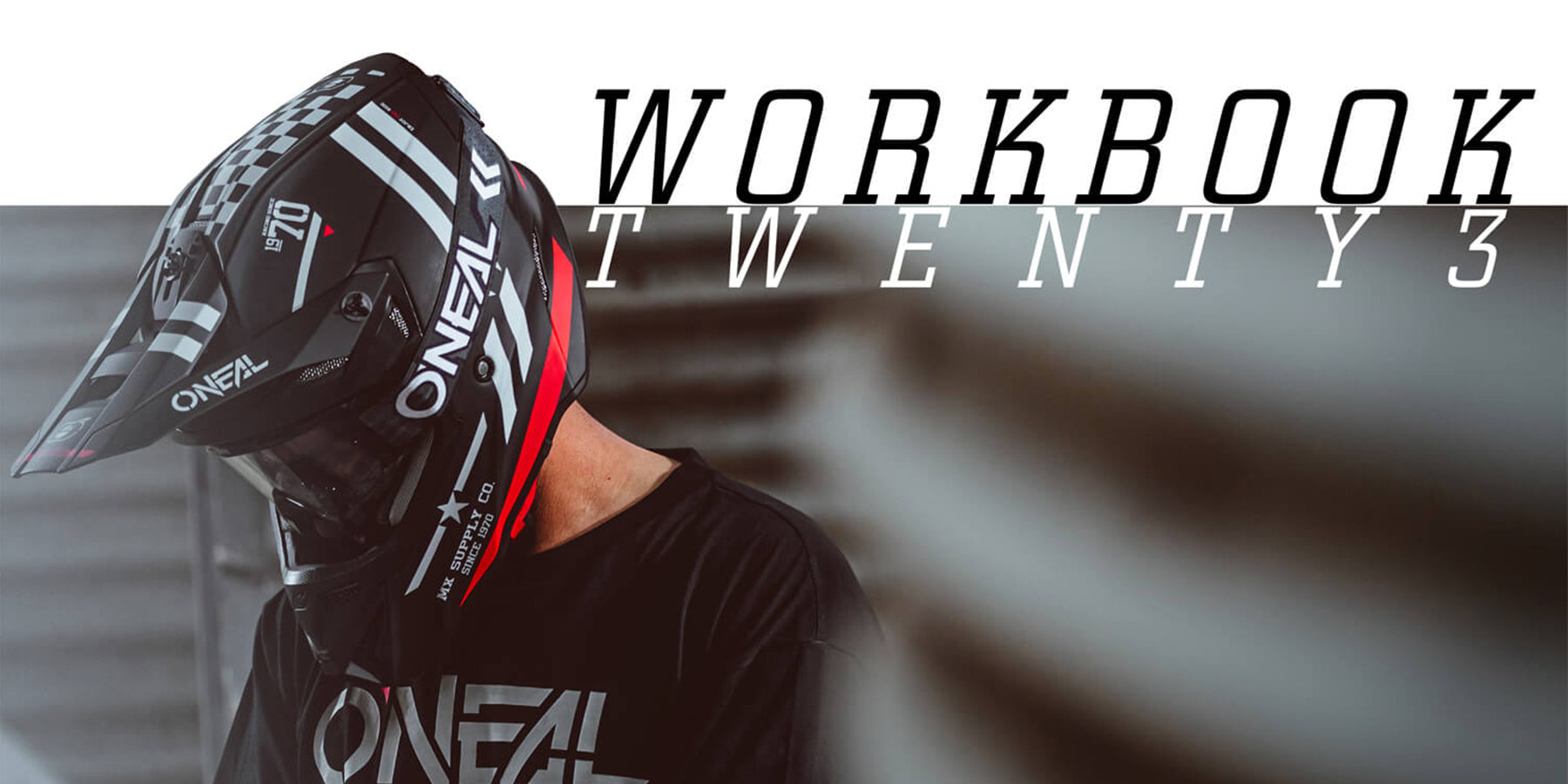 Eine Person mit einem schwarzen O'Neal-Motocrosshelm und einem schwarzen O'Neal-T-Shirt blickt nach unten. In der oberen rechten Ecke wird auf weißem Hintergrund der Text „WORKBOOK TWENTY3“ angezeigt.